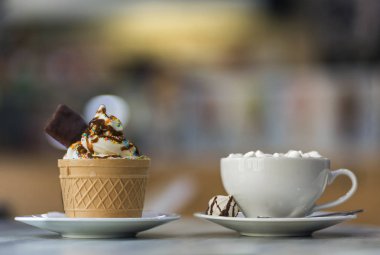 Gofret fincan çikolatalı kurabiye ile dondurma tatlı ve ve bulanık renkli kopya alanı zemin üzerine porselen tabakta marshmallow ile kahve bir fincan.