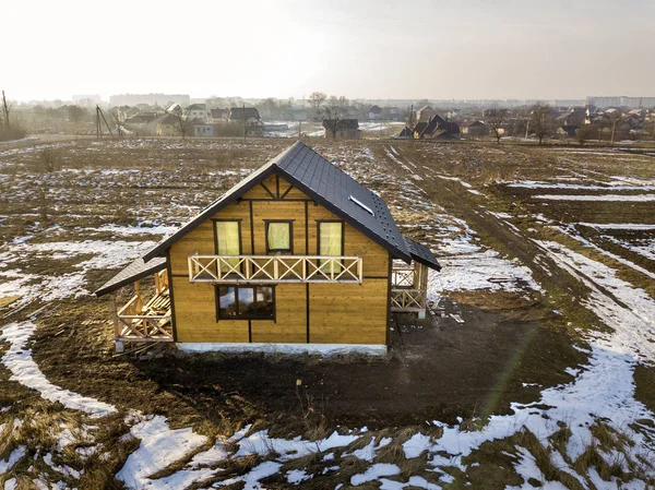 Aerial view of new wooden ecological traditional house cottage of natural lumber materials with steep shingle roof under construction on winter rural landscape background. — Stock Photo, Image