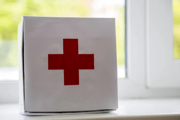 White first aid kit with red cross indoors on windowsill on blur — Stock Photo, Image