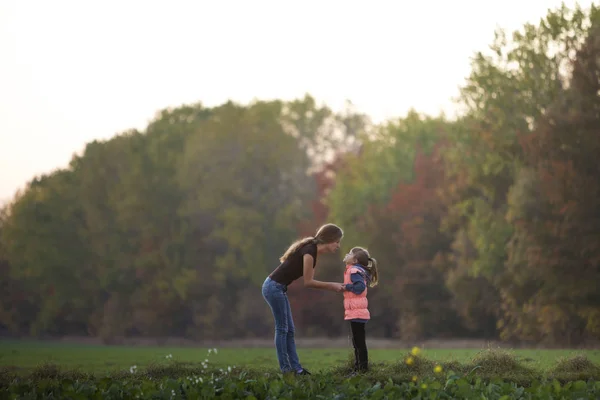 Perfil de larga duración retrato de la joven madre atractiva delgada hablando con la niña de pie en el prado verde de la mano al aire libre en los árboles del bosque fondo borroso . — Foto de Stock