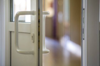 Bulanık iç arka plan üzerinde metal kilit, kulp ve şeffaf cam ile beyaz plastik kapı detay. Kurulum ve tasarım konsepti.