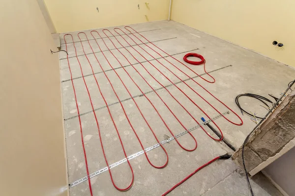 Отопление красный электрический провод монтаж на цементном полу в маленькой новой незаконченной комнате с гипсовыми стенами. Реконструкция и строительство, концепция комфортного теплого дома . — стоковое фото