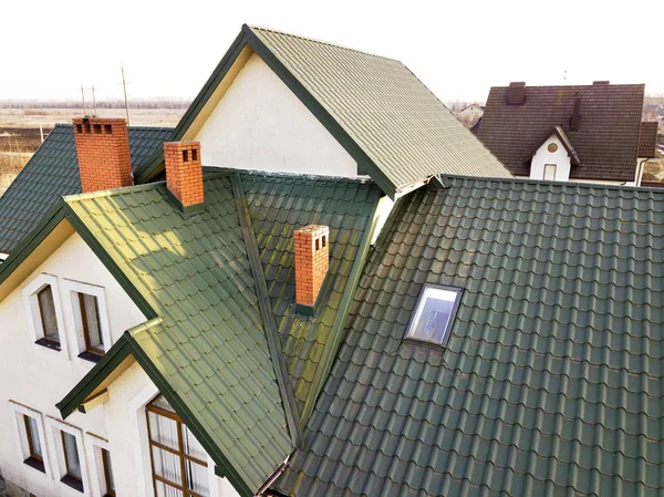 Green metal shingled house roof with attic plastic window and br