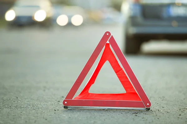 Red emergency triangle stop sign and broken car on a city street