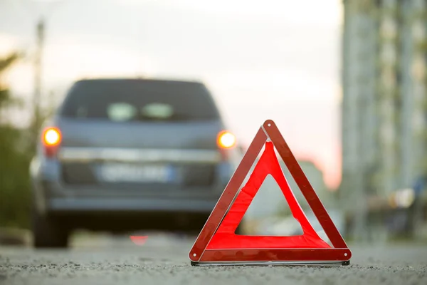 Red emergency triangle stop sign and broken car on a city street