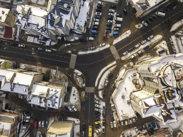 Aerial black and white winter top view of modern city with tall buildings, parked and moving cars along streets with road marking. Urban cityscape, view from above.