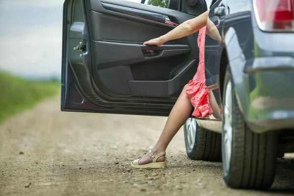 Jovem mulher em vestido curto saindo do carro com porta aberta em ensolarado desfocado rural estrada fundo . — Fotografia de Stock