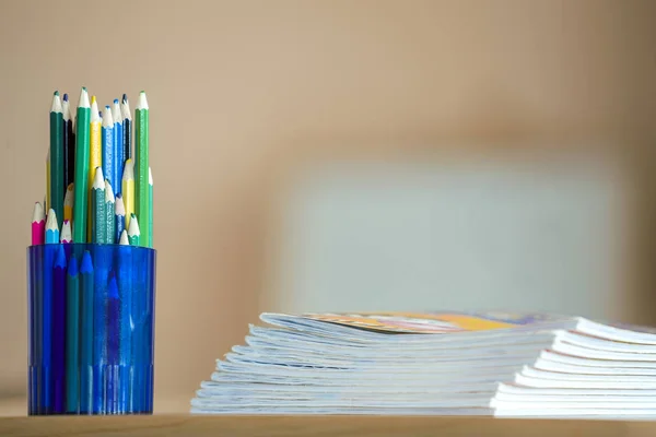 Wooden colorful drawing pencils arranged in plastic jug and stack of copybooks on light copy space background. — Stock Image Wooden colorful drawing pencils arranged in plastic jug and stack of copybooks on light copy space background. Stock Image