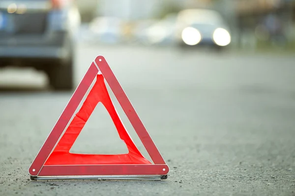 Red emergency triangle stop sign and broken car on a city street