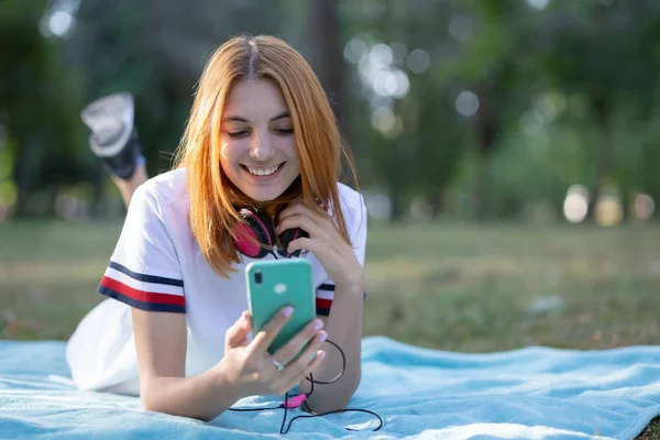 Bastante sonriente adolescente con el pelo rojo usando sellphone outdoo —  Fotos de Stock