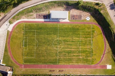 Yeşil kaplı bir stadyumdaki futbol sahasının havadan görünüşü. 