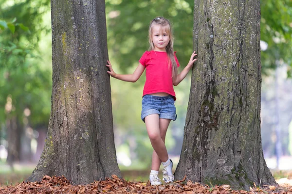 Porträtt av en söt liten flicka som står nära stora träd tr — Stockfoto