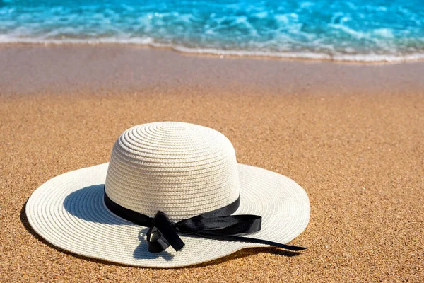 White woman straw hat laying on tropical sand beach with blue vibrant ocean water in background on sunny summer day. Vacations and destination travel concept.
