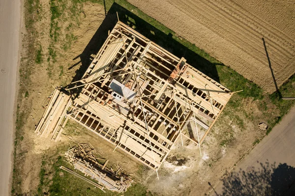 Aerial view of unfinished brick house with wooden roof frame structure under construction.