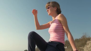Genç, rahat bir kadın büyük bir taşın üzerinde oturmuş sıcak bir yaz gününün tadını çıkarıyor. Gün batımında meditasyon yapan ve dinlenen bir kız..