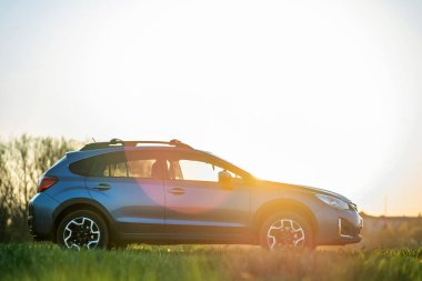Gün batımında yeşil çimlerin üzerinde mavi arazi arabası. Otomobille seyahat, vahşi yaşam macerası, keşif gezisi ya da bir SUV otomobili ile aşırı seyahat. Offroad 4x4 aracı gün doğumunda arazide olacak..
