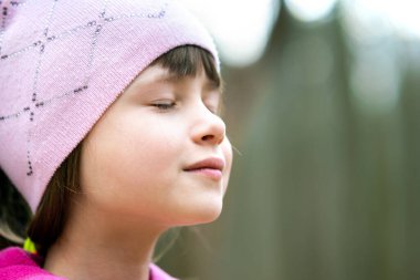 Pembe ceketli ve şapkalı güzel bir kızın portresi. Baharın erken saatlerinde açık havada güneşli bir günün tadını çıkarıyor..