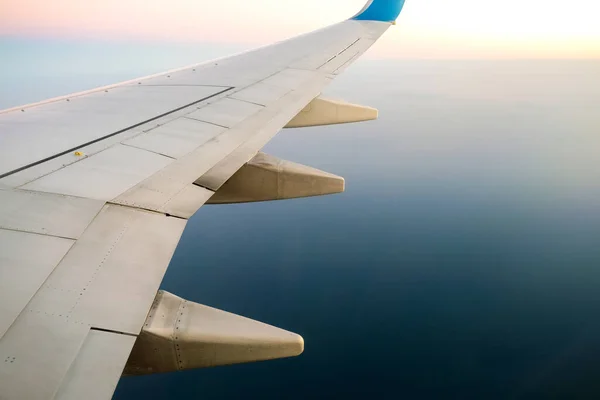 View from airplane on the aircraft white wing flying over ocean landscape in sunny morning. Air travel and transportation concept.