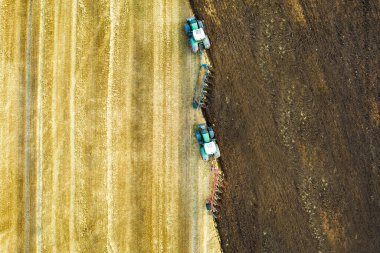 Sonbaharda hasattan sonra siyah tarım tarlasını süren bir traktörün hava görüntüsü.