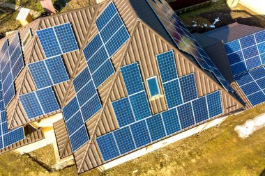 Çatıda mavi parlak güneş enerjili voltaik panelleri olan yeni, modern ev kulübesinin havadan görünüşü. Yenilenebilir ekolojik yeşil enerji üretim kavramı.