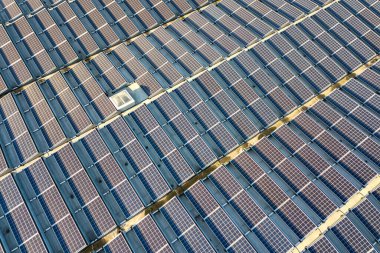 Sanayi binasının çatısına monte edilmiş birçok voltaik güneş panelinin hava görüntüsü.