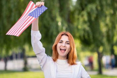 Yaz parkında Amerikan bayrağıyla poz veren mutlu genç bir kadın. Açık havada afişi olan pozitif kız..