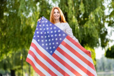 Yaz parkında Amerikan bayrağıyla poz veren mutlu genç bir kadın. Açık havada afişi olan pozitif kız..