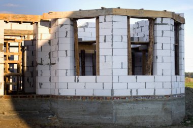 İnşaat halindeki ev, havalandırılmış beyaz köpük duvarlar beton bloklar, ahşap iskeleler, büyük pencere açıkları ve beton temeller..