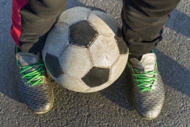 Güneşli bir günde spor ayakkabılı çocuk bacaklarının açık havada futbol topu tutması. Gençlerin tatil aktiviteleri, spor ve eğlence konsepti.