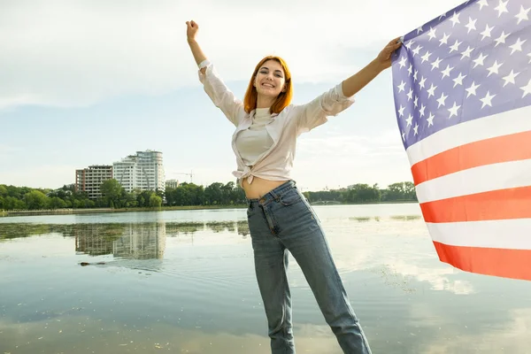 Happy red haired woman with United States national flag in her hand. Positive girl celebrating US independence day.