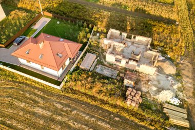 İki özel evin yukarıdan aşağı görüntüsü, biri beton temeli ve tuğla duvarlı, diğeri de kırmızı kiremitli çatıyla bitirilmiş..
