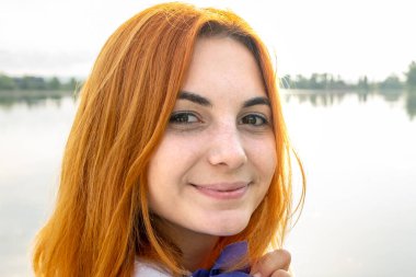 Gülümseyen kızıl saçlı kızın portresi. Dışarıdaki kameraya bakan pozitif genç bir kadın..