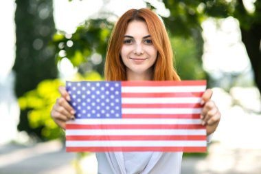 Amerikan bayrağıyla poz veren mutlu genç bir kadın onu açık havada, yaz parkında tutuyor. Güzel kız Amerika 'nın bağımsızlık gününü kutluyor. Uluslararası Demokrasi Günü.