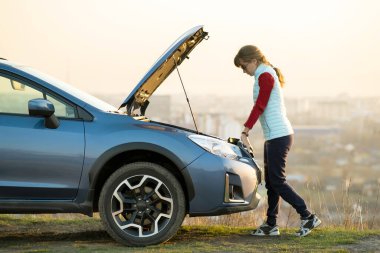 Kaputu patlamış, bozuk bir arabanın yanında duran genç bir kadın aracıyla sorun yaşıyor. Otomatik arıza dışında yardım bekleyen kadın sürücü.