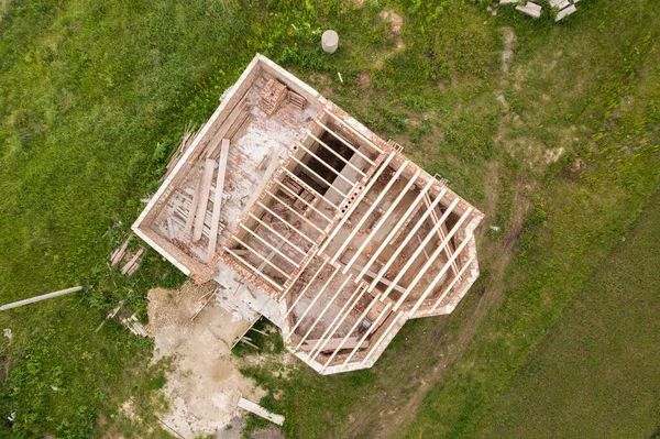 Aerial view of a brick house with wooden ceiling frame under construction.