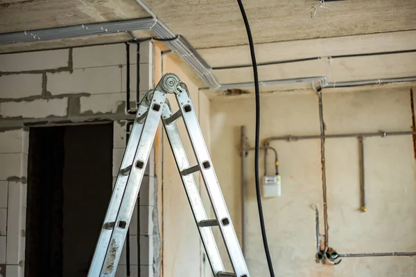 Alüminyum merdiven ve elektrik kabloları inşaat halindeki bir odanın tavanına ve duvarına yerleştirilmiş koruyucu korkuluklara yerleştirilmiş..