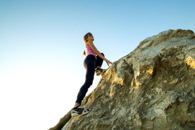 Güneşli bir günde kadın yürüyüşçü dik kayalara tırmanıyor. Genç bayan dağcı zor tırmanma rotasının üstesinden gelir. Doğada aktif eğlence kavramı.