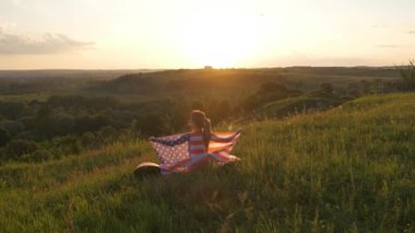 Gün batımında ABD bayrağıyla poz veren genç bir kadın. ABD 'nin bağımsızlık gününü kutlayan pozitif kız.