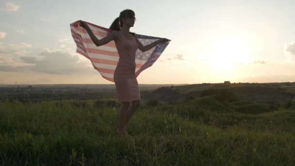 日没時にアメリカ国旗を屋外でポーズしている幸せな若い女性のバックビュー アメリカ独立記念日を祝う正の少女 民主主義の国際デー — ストック動画