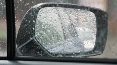 Dikiz aynasına yakın, yağmur damlaları arabanın ön camına düşüyor..
