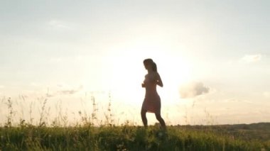 Açık renk elbiseli, uzun saçlı genç bir kadın ılık günbatımında yaz çayırında koşuyor..