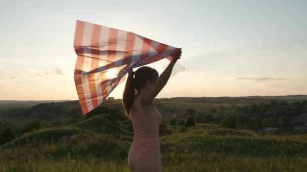 日没時にアメリカ国旗を屋外に立ってポーズをとっている幸せな若い女性 アメリカ独立記念日を祝う正の少女 民主主義の国際デー — ストック動画