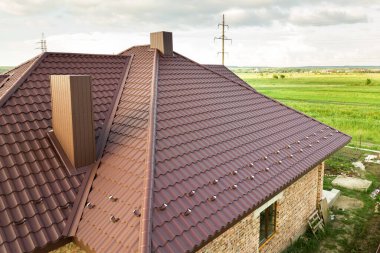 Kahverengi metal kiremitlerle kaplı evin çatı yapısının havadan görünüşü.
