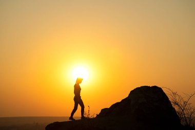 Gün batımında dağlarda büyük bir kayaya tırmanan bir kadın yürüyüşçünün silueti. Akşam vakti yüksek kayalıklarda gezen kadın turist. Turizm, seyahat ve sağlıklı yaşam tarzı konsepti.