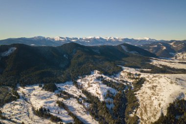 Kışın karla kaplı tepelerde dağınık evleri ve Ukrayna 'daki çıplak karanlık Karpat dağları olan küçük bir köyün havadan görünüşü..