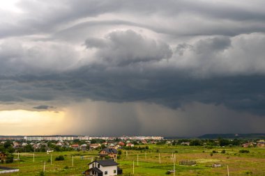 Kara fırtınalı bulutlarla kapkara bir manzara Yazın uzak kasaba binalarının üzerine sağanak yağmur yağıyor.