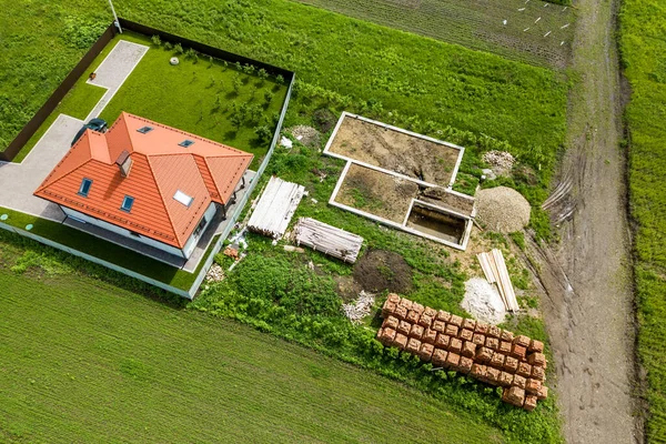 Aerial view of building site for future brick house, concrete foundation floor and stacks of yellow clay bricks for construction.