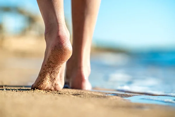 Close up of woman feet walking barefoot on sand leaving footprints on golden beach. Vacation, travel and freedom concept. People relaxing in summer.