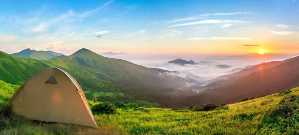 Tourist tent located in summer mountains at sunset. Hiking camp in evening nature. Travel and get away concept.