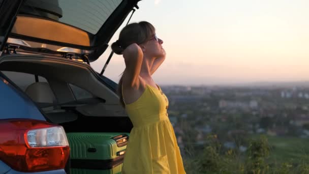 幸せな若い女性は彼女の車の近くに夕日を楽しむ立っている 旅行と休暇のコンセプト — ストック動画